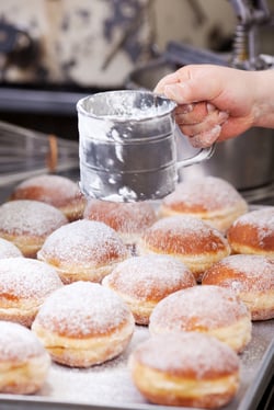 Baker is poring powdered sugar over doughnuts