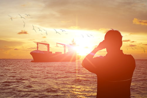 Man watching cargo ship at sunset