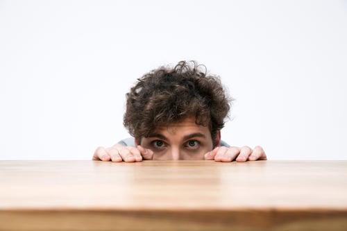 Young man with curly hair peeking from behind the desk