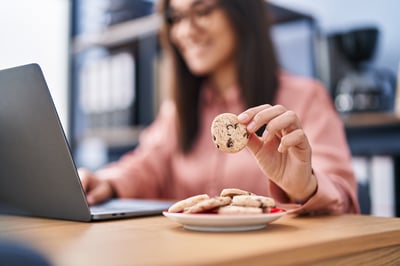 woman eating cookies at the computer while working with API solutions